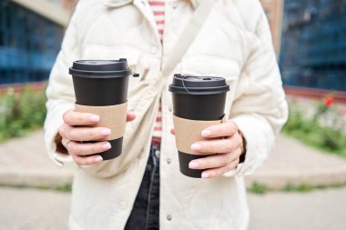 Mahalledeki bir kız elinde kahve bardakları tutuyor. Genç bir kadının elinde iki bardak sıcak içecek. Kahvaltı hazırda bekliyor. Piknik ve dışarı çıkma konsepti. - Evet. Yüksek kalite fotoğraf