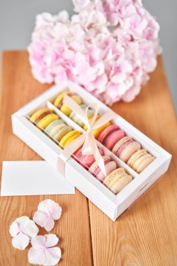 Mesaj için beyaz kart. Mevcut kutuda Fransız makarnası var. Çiçek arkaplanda tatlı bir tatlı. Makarna kekleri ve farklı çiçeklerle dolu bir hayat. Teslimat konsepti, kahve ve çiçekçi. Yüksek