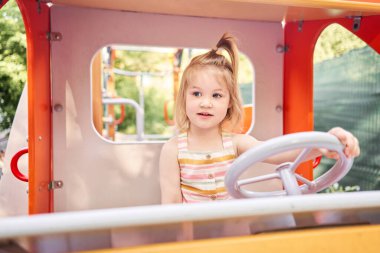 Oyun oynayan küçük bir kız, çocuk parkında direksiyon tutan bir araba şoförü. Güneşli bir yaz akşamı, eğlenceli bir çocukluk. Yüksek kalite fotoğraf