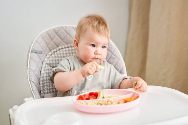 Tatlı çocuk sağlıklı makarna ve sebze buğulama yiyor. 10 aylık güzel bir kızın portreleri. Bebek bebekler için özel bir sandalyede oturuyor. Yüksek kalite fotoğraf