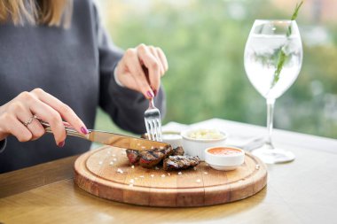 Bir restoranda öğle yemeği, bir kadın ızgarada pişmiş ciğer parçaları yer. Tahta bir tahtanın üzerinde hizmet veriyor. Barbekü restoranının menüsü, bir dizi farklı etin fotoğrafları. Yüksek kalite fotoğraf