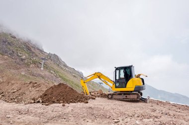 Kazıcı dağlık arazide çalışıyor. İletişim için siper kazıyor. Su ve elektrik. Dağların eteğinde. Bir yolun tamiri ve genişletilmesi. Yüksek kalite fotoğraf