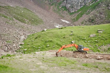 Kazıcı dağlık arazide çalışıyor. Dağların eteğindeki bir çamur kaymasının sonuçlarını temizler. Bir yolun tamiri ve genişletilmesi. Yüksek kalite fotoğraf