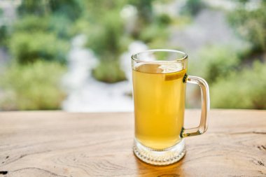 Bir bardak limonlu zencefil kökü çayı, bal ve nane arkaplanda yüksek dağ nehri ve ahşap bir masa üzerinde. Dağlarda yürü ve rahat bir kafede rahatla. İzin gününde yürüyüş yapmak. Yüksek kalite fotoğraf