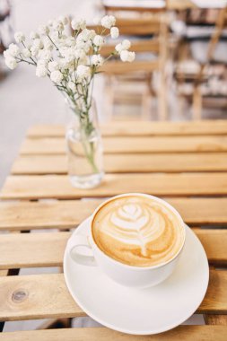 Bir fincan sıcak kapuçino. Kahve dükkanının ortak çalışma alanındaki masa. Güneşli bir günde verandada bir fincan kahve. Kafede kahve molası. Yakın plan. Yüksek kalite fotoğraf.