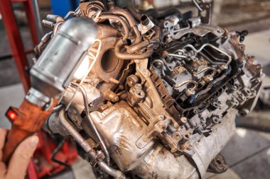 Bir araba tamircisi el feneriyle motoru inceliyor. Motor bloğu, özel vinç krikosuyla birlikte tamir masasında. Araba için teknik servis istasyonu yüksek kaliteli fotoğraf.