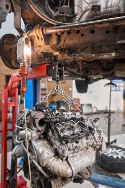 Bir araba tamircisi el feneriyle motoru inceliyor. Motor bloğu, özel vinç krikosuyla birlikte tamir masasında. Araba için teknik servis istasyonu yüksek kaliteli fotoğraf.