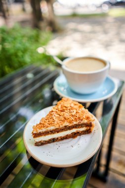 Bir fincan sıcak Peanut latte ve havuçlu kek. Kahve dükkanının ortak çalışma alanındaki masa. Güneşli bir günde verandada bir fincan kahve. Kafede kahve molası. Yakın plan. Yüksek kalite fotoğraf.