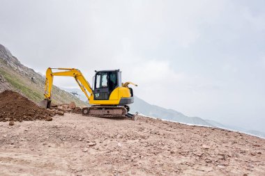 Kazıcı dağlık arazide çalışıyor. İletişim için siper kazıyor. Su ve elektrik. Dağların eteğinde. Bir yolun tamiri ve genişletilmesi. Yüksek kalite fotoğraf