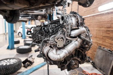 Bir araba tamircisi el feneriyle motoru inceliyor. Motor bloğu, özel vinç krikosuyla birlikte tamir masasında. Araba için teknik servis istasyonu yüksek kaliteli fotoğraf.