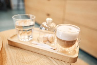 Bir fincan cantuccini ve ahşap tepside bir bardak su. Sütlü kahve, kurabiye ve cam sehpanın üzerinde su olan bir bardak. Yüksek kalite fotoğraf