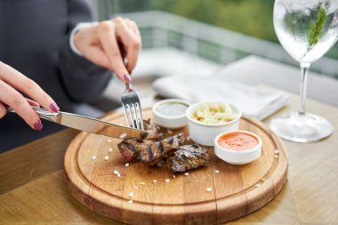 Bir restoranda öğle yemeği, bir kadın ızgarada pişmiş ciğer parçaları yer. Tahta bir tahtanın üzerinde hizmet veriyor. Barbekü restoranının menüsü, bir dizi farklı etin fotoğrafları. Yüksek kalite fotoğraf