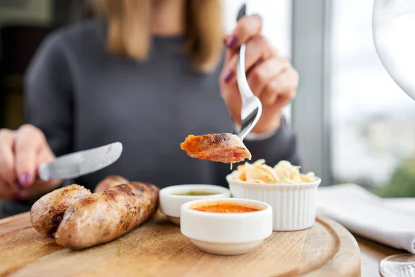 A piece of sausage is dipped in sauce. Lunch in a restaurant, a woman cuts Grilled sausages. Barbecue restaurant menu, a series of photos of different means. High quality photo