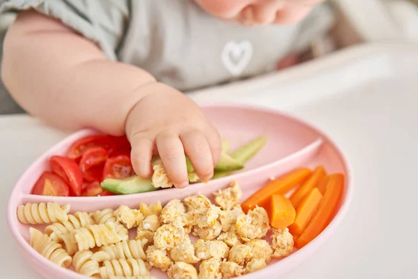 Cute child eats healthy food pasta and vegetables steamed,. Portraits of a cute 10 months old baby girl. The baby sitting in a special high chair for babies. High quality photo