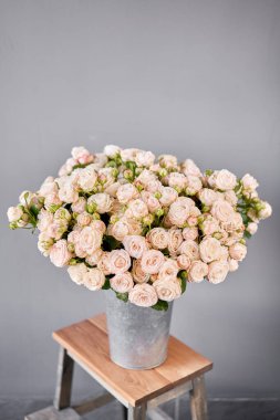 Alüminyum vazo ve çalılık gülleri. Çiçeklerle çiçekçi ilgileniyor. Elinde bir vazo çiçek olan bir kız yüksek kaliteli bir fotoğraf.