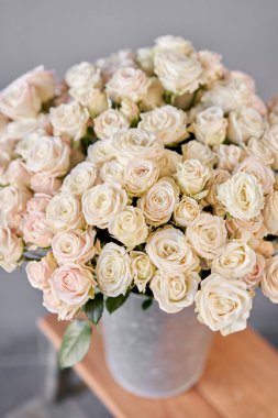 Alüminyum vazo ve çalılık gülleri. Çiçeklerle çiçekçi ilgileniyor. Elinde bir vazo çiçek olan bir kız yüksek kaliteli bir fotoğraf.