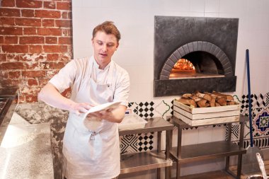 Şef pizza hazırlar. Çiğ pizza pişirmeye hazır. Mutfakta önlüklü aşçı pizza hamuru yapıyor. Arka planda yiyecek teslimatı için kutular. neopolitan