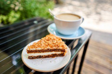 Bir fincan sıcak Peanut latte ve havuçlu kek. Kahve dükkanının ortak çalışma alanındaki masa. Güneşli bir günde verandada bir fincan kahve. Kafede kahve molası. Yakın plan. Yüksek kalite fotoğraf.