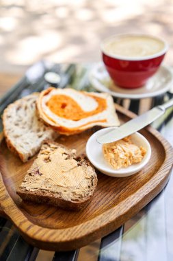 Tahtada dilimlenmiş ekmek. Tütsülenmiş tereyağı ile servis edilir. Cappuccino kahveli kahvaltı. Ahşap tabakta tereyağı ve ekmek kompozisyonu. Yüksek kalite fotoğraf