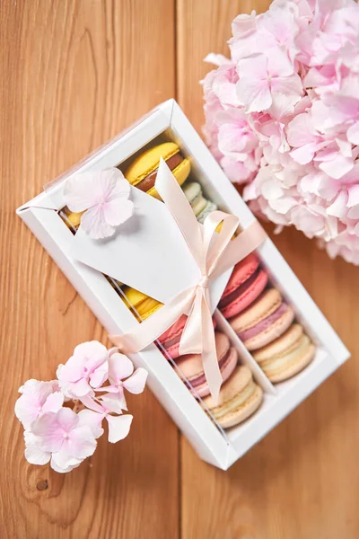 Dessert French Macarons in present box. Sweet dessert on a flowers background. Still life with macaroni cakes and different flower. Delivery concept, coffee and flower shop. High quality photo