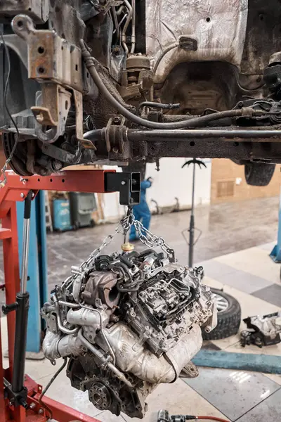 A car mechanic inspects the engine with a flashlight. Engine Block on a repair stand with Special crane jack. Technical service station for car.. High quality photo