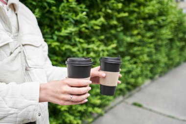 Mahalledeki bir kız elinde kahve bardakları tutuyor. Genç bir kadının elinde iki bardak sıcak içecek. Kahvaltı hazırda bekliyor. Piknik ve dışarı çıkma konsepti. - Evet. Yüksek kalite fotoğraf