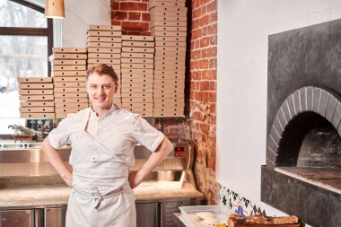 Şef Napolitan pizzacıda pizza hazırlıyor. Mutfakta elinde kürekle önlük içinde yemek pişiriyor. Arka planda yiyecek teslimatı için kutular. Yüksek kalite fotoğraf