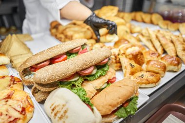 Taze sandviç, turta ve pizza bir kafe, açık büfe veya self-servis kafe vitrininde tercih edilebilir. Jambonlu ve peynirli kruvasan. Kafedeki rafta sıcak hamur işleri var. Çörekler dükkanda. Yüksek