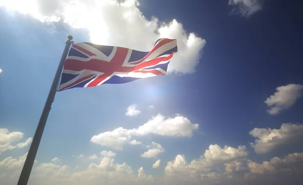 UK Flag waving on a Flagpole in front of a blue sky with clouds