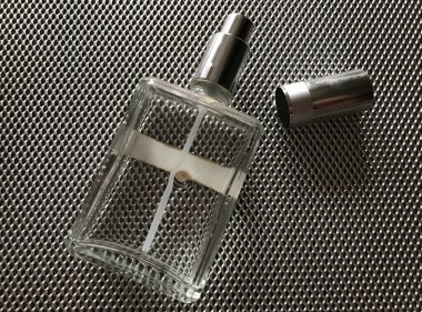 Transparent perfume spray bottle on steel mesh background