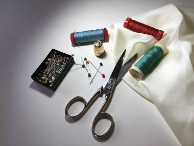 Scissors, threads, pins and white fabric
