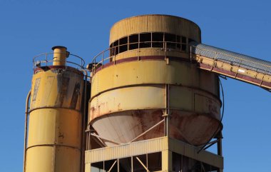 Gökyüzünün uçsuz bucaksız genişliğine karşı yükselen sarı fabrikanın istikrarlı varlığına bakın.