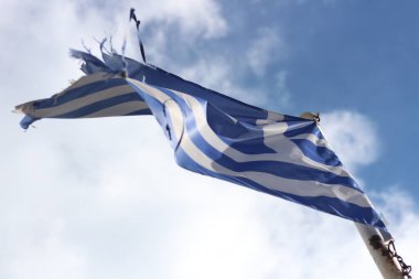 Behold the symbol of resilience and unwavering pride as a weathered Greek flag flutters against the backdrop of a clear blue sky clipart