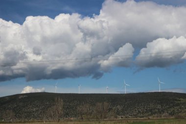 Against a backdrop of fluffy clouds and radiant sunshine, wind turbines stand tall, their blades slicing through the air to harness clean, renewable energy clipart