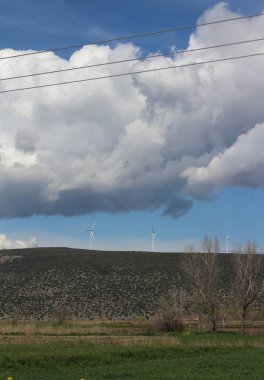 Pofuduk bulutların ve parlak güneş ışığının zemininde rüzgâr türbinleri dik duruyor. Temiz ve yenilenebilir enerjiyi elde etmek için bıçakları havayı kesiyor.