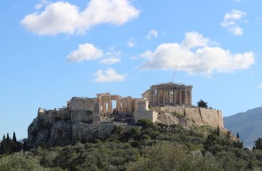 Gök mavisi genişliğinde, Akropolis yazın sıcacık kucağında güneşleniyor, turistleri antik harikalarını keşfetmeye çağırıyor pofuduk bulutların arasında.