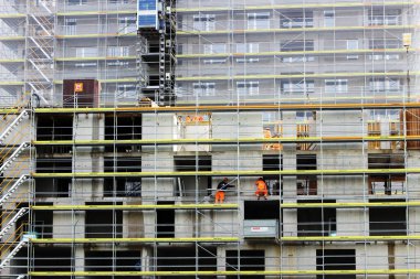 Zürih 'in gayretli ruhunu yakalayan bu resimde çalışanlar, şehrin sürekli değişen gökyüzü ve kentsel manzarasına katkıda bulunan bir yapı iskelesi üzerinde özenle görevlerini yerine getiriyorlar.