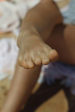 Bir Yunan plajının sıcak, altın kumsalına kurulmuş bir çift dişi ayak parmağı, güneşin altında parlayan tahıllarla şakayla süslenmiş. Bu yakın çekim rahatlama ve sevincin özünü yakalar.