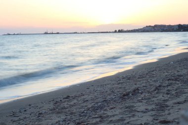 Günbatımı, deniz ve kumda sıcak, altın bir parıltı bırakır ve su yüzeyinde dans eden büyüleyici bir yansıma yaratır. Turuncu ve pembe renklerin dingin mavilerle harmanlanması gibi.