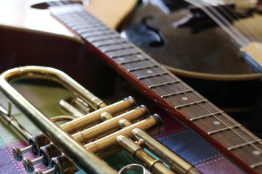 Akustik gitar, mandolin ve trompetin yakın plan görüntüsü, her enstrümanın farklı doku ve tonlarını yakalar.