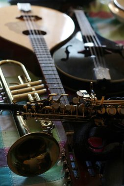 Bir akustik gitar, mandolin ve saksafon yakın çekim yan yana dizilmiş, ahşap telli enstrümanların toprak sıcaklığını yakalıyor
