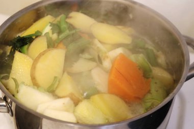 Patates, balkabağı ve taze yeşillikler içeren canlı, buharda pişmiş bir sebze çorbası.