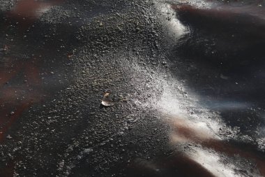 Kirlenmiş bir su yüzeyinin çarpıcı bir görüntüsü turuncu, siyah ve kahverengi tonlarında dönen yağlı desenleri gösteriyor.