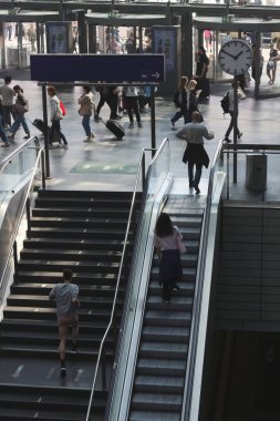 Dinamik çekimler, Almanya 'nın en işlek demiryolu istasyonu Berlin Hauptbahnhof' un canlı atmosferini yakalıyor. İnsanlar modern mimarisinde hızla ilerliyorlar.