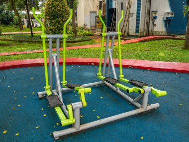 Two lime green Cross Trainer fitness equipment placed outdoor on a blue surface at a public park.