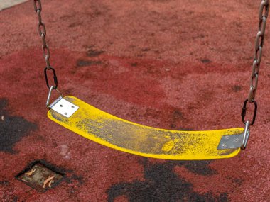 An aged yellow polymer belt swing seat with a pair of iron chains and hooks at a public park.