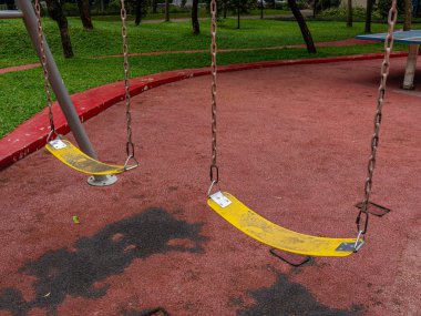 Two yellow polymer belt swing seats with chains and hooks at a public park.