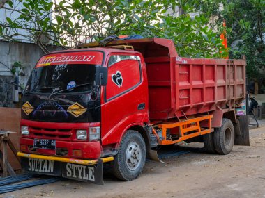 Banten, Indonesia - August 9, 2022: A bright red common dump truck parking under a tree with a writing saying 