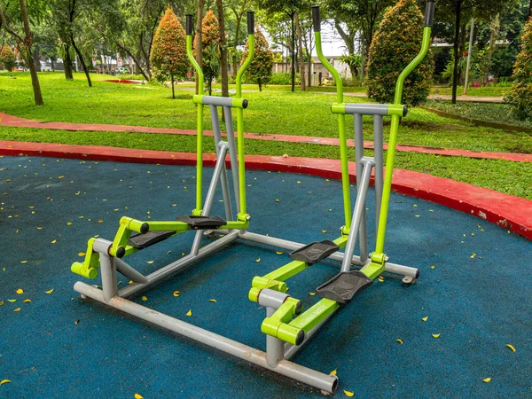 A pair of lime green Cross Trainer fitness equipment placed at an outdoor public park during a sunny morning.