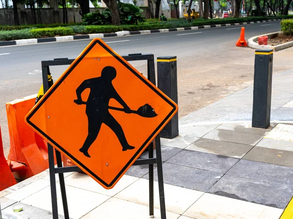 An orange construction traffic sign placed on a sidewalk during empty traffic.
